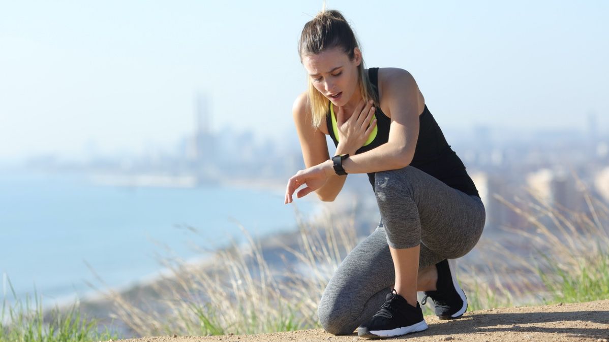 Junge Frau in Sportkleidung greift sich an die Brust und schaut auf eine Smartwatch 