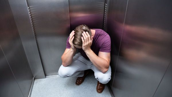 Junger Mann hockt verzweifelt in einem Fahrstuhl.