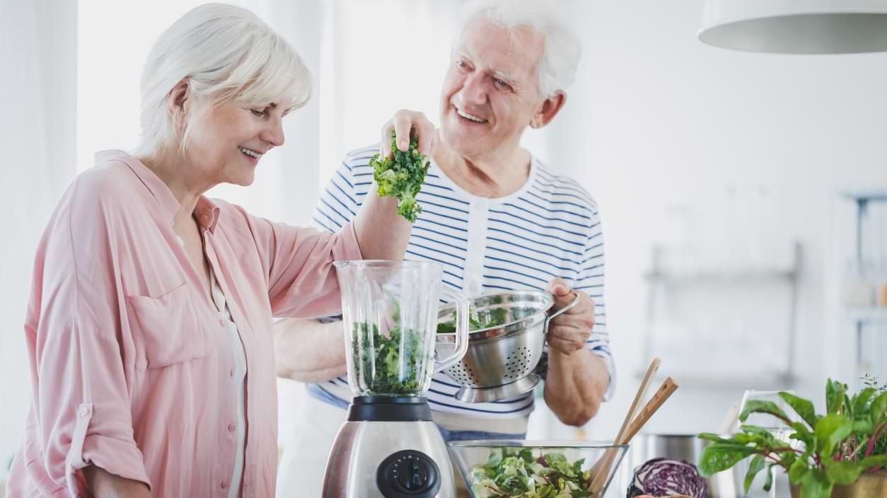 Zwei alte Menschen mixen einen grünen Gemüsesmoothie 
