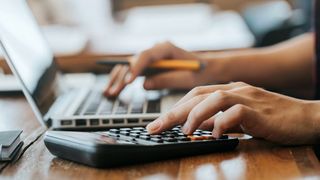 Hände halten einen Stift und tippen auf Laptop und Taschenrechner, um das Gehalt in der Verwaltung als Mitarbeiterin bzw. Mitarbeiter auszurechnen. 