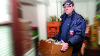 Ein Malteser Helfer trägt einen Karton mit Lebensmitteln