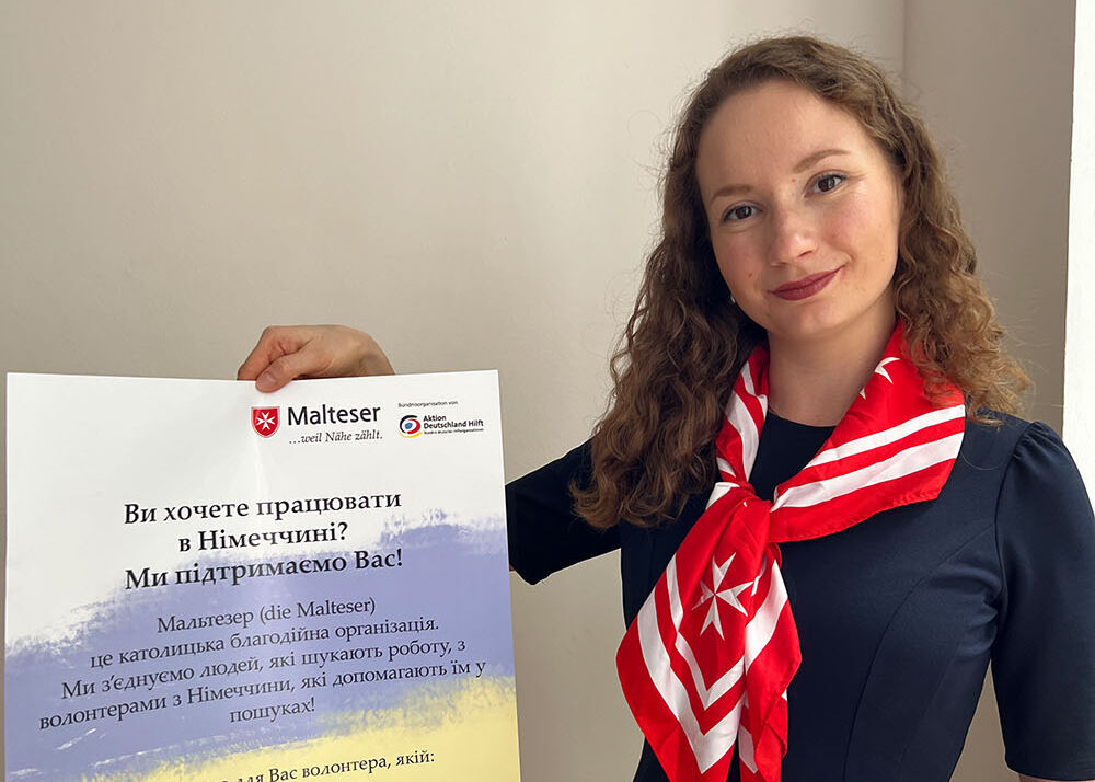 Zarina Gatina, die für die Ukraine-Hilfe zuständige Ehrenamtskoordinatorin, präsentiert das Plakat, mit dem die Münchner Malteser über ihr Jobmentoring-Programm informieren.