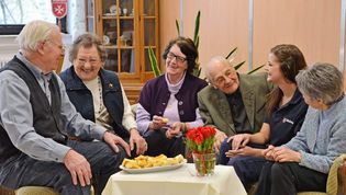 Senioren sitzen gemütlich im Café Malta mit einer Malteser Mitarbeiterin.