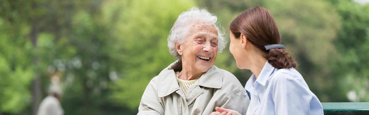 Altenpflege: Junge Frau sitzt mit älteren Dame auf einer Parkbank
