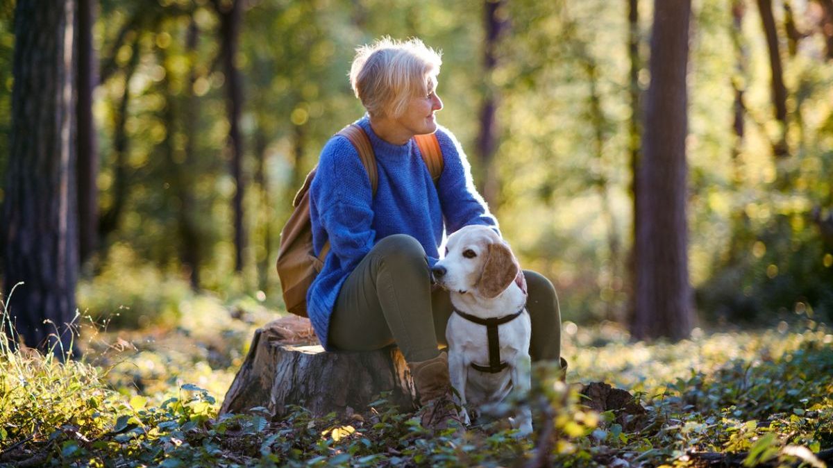 Eine ältere Frau mit Hund in einem Wald.