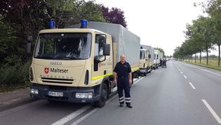 Malteser Mitarbeiter steht vor einer Fahrzeugkolonne mit Malteser Einsatzfahrzeugen