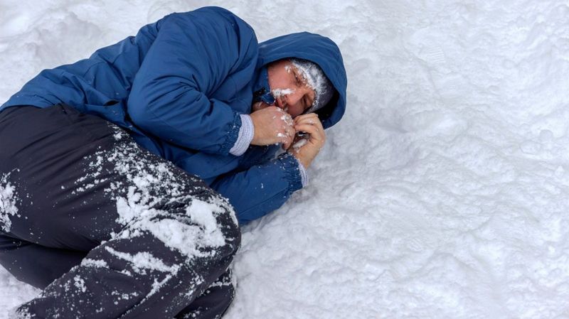 Ein Mann mit einer blauen Winterjacke liegt zusammengerollt im Schnee