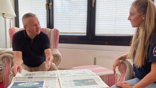 Eine Junge Frau spricht mit einem älteren Mann, der eine Zeitung durchblättert.
