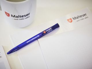 Kugelschreiber, Tasse und Papier mit Malteser Logo