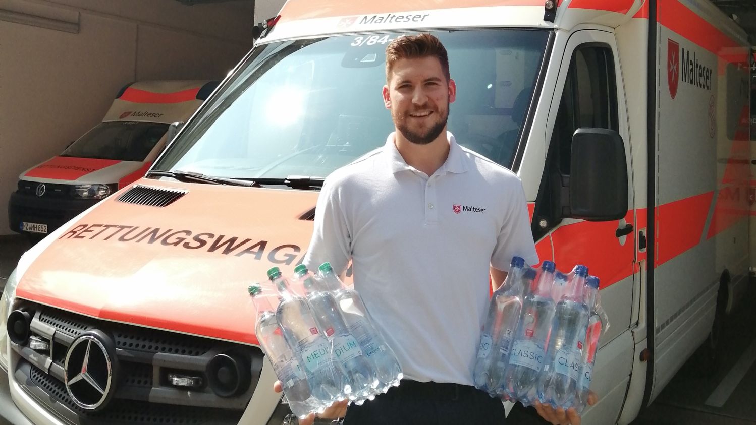 Junger Mann mit Wasserflaschen vor Rettungswagen