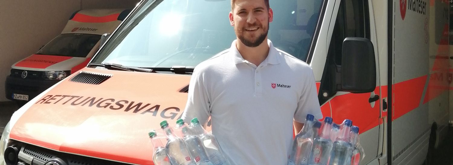 Mann mit Wasserflaschen vor Rettungswagen 