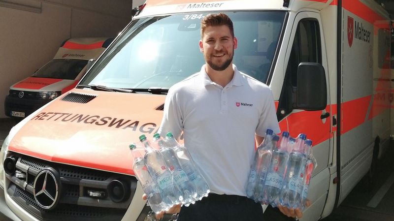 Ein junger Mann vor einem Rettungswagen mit Wasserflaschen in beiden Armen. 