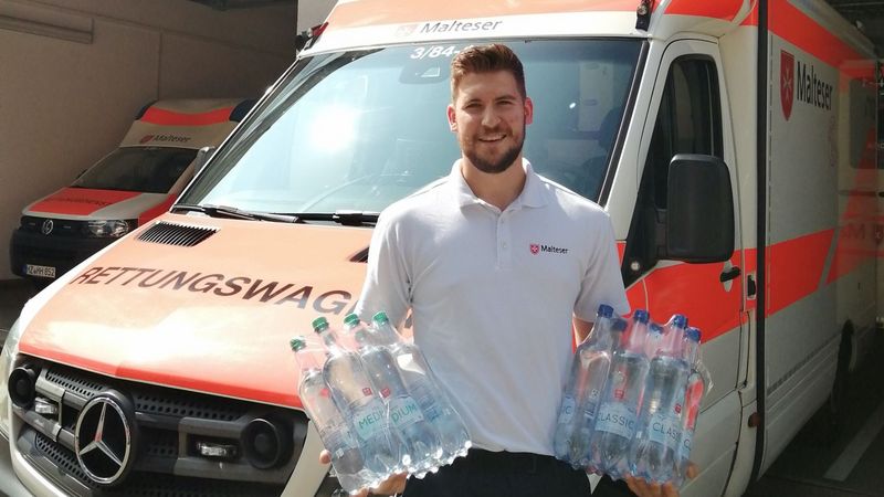 Junger Mann mit Wasserflaschen vor einem Rettungswagen