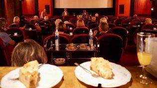 Zwei Kuchen im Vordergrund, ein Kinosaal mit Zuschauern im Hintergrund.