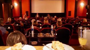 Zwei Kuchen im Vordergrund, ein Kinosaal mit Zuschauern im Hintergrund.