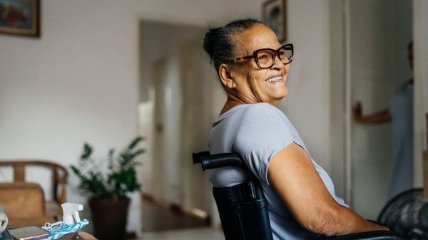 Eine lächelnde, ältere Frau mit großer Brille in einem Rollstuhl.