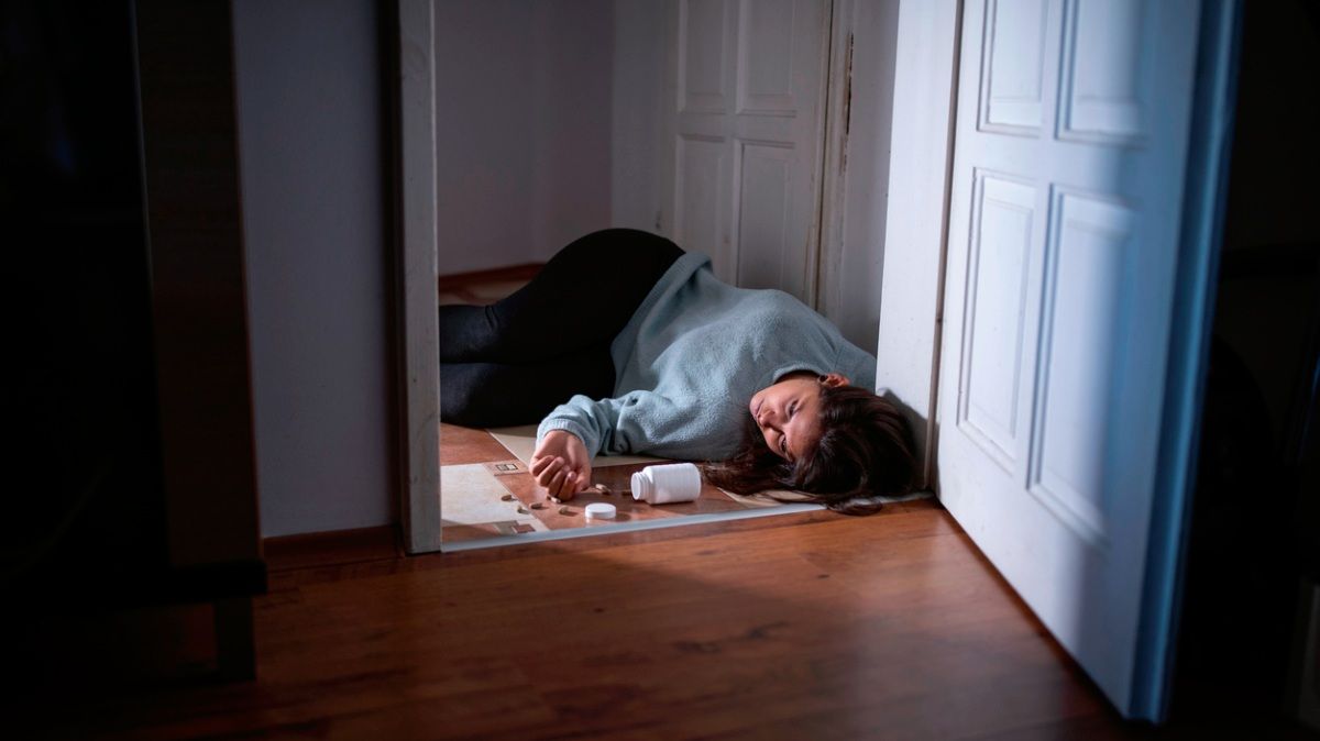 Eine bewusstlose Frau liegt auf dem Boden neben einer geöffneten Pillendose.