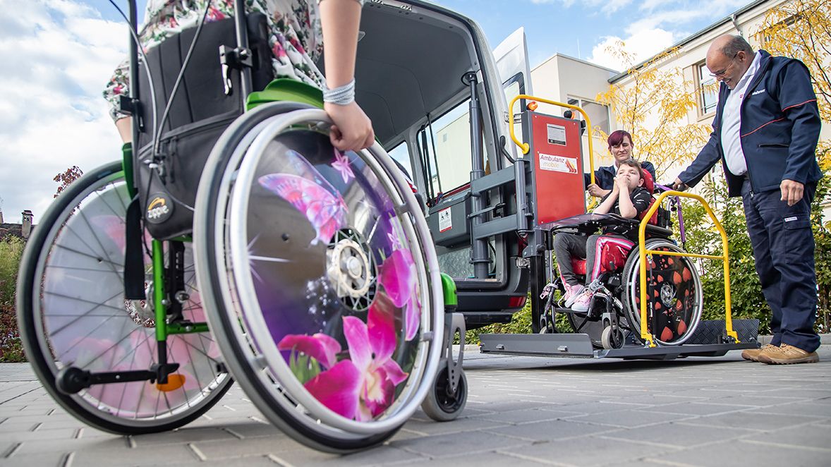 Fahrdienstmitarbeiter der Malteser helfen Kindern im Rollstuhl.