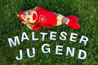 Ritter Malte Puppe liegt auf einer Wiese mit dem Schriftzug Malteser Jugend darunter.