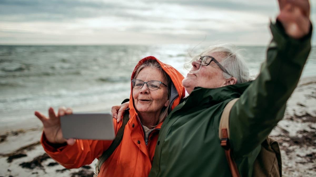 Zwei ältere Damen machen einen Strandspaziergang und fotografieren sich.