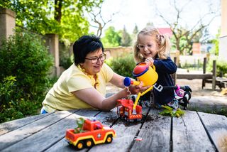 Eine Mutter spielt mit ihrer kleinen Tochter mit Plastikspielzeug auf einem Spielplatz-Outdoor-Holztisch.