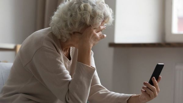 Es ist eine traurige ältere Dame zu sehen, welche auf ihren Tablet schaut.