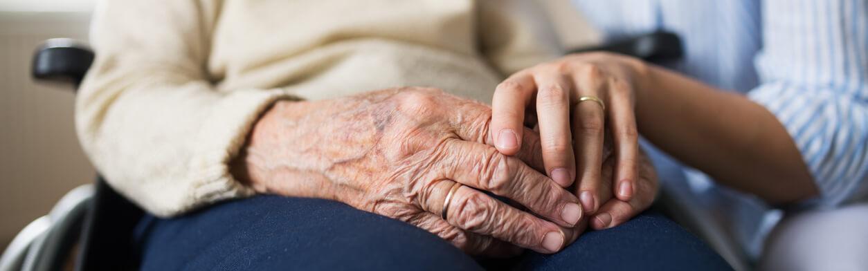 Eine ambulante Pflegekraft hält die Hand einer Seniorin im Rollstuhl.