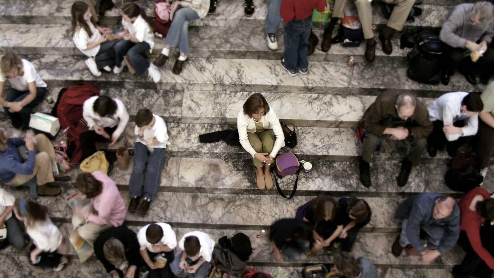 Gruppe von Menschen sitzen auf einer Treppe, eine Person sitzt isoliert