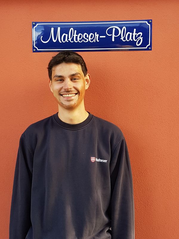 Junger Mann unter einem Schild mit der Aufschrift „Malteser-Platz“