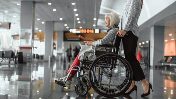 Es wird eine ältere Dame im Rollstuhl am Flughafen gezeigt.