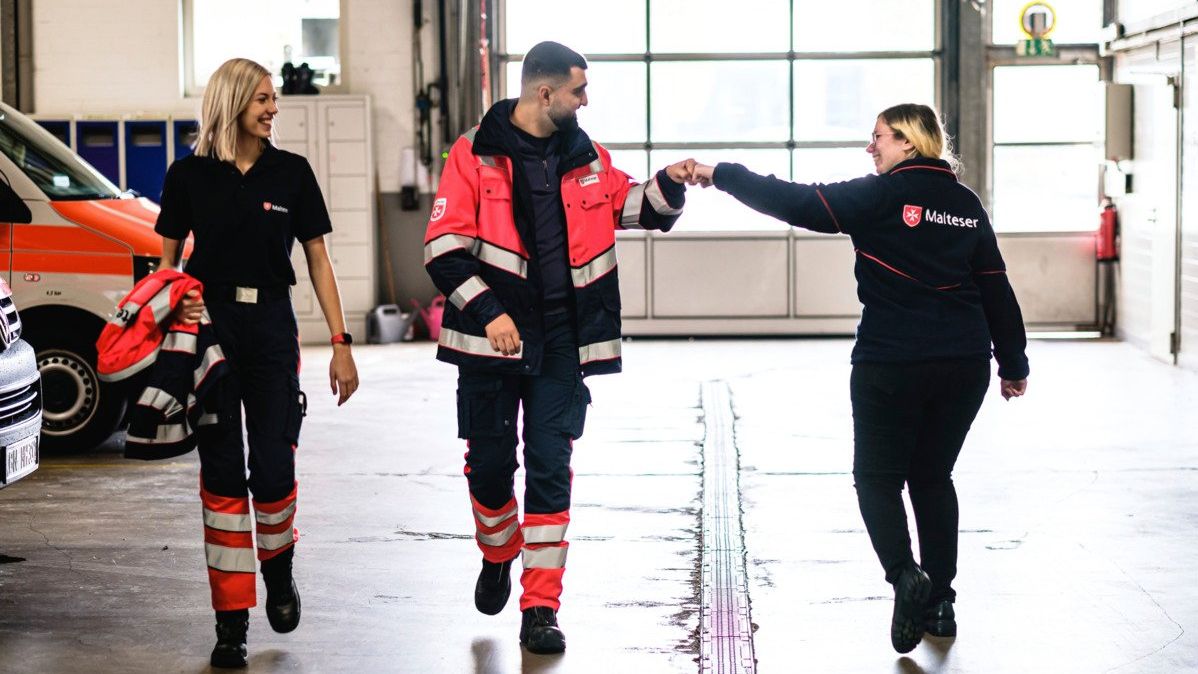 Junge, lächelnde Freiwillige der Malteser in Deutschland geben sich im Vorbeigehen einen Fistbump