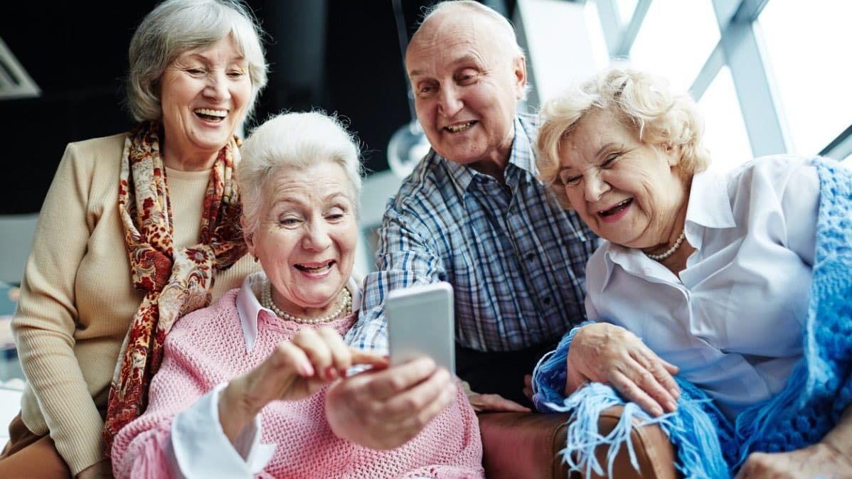 Mehrere Senioren schauen lachend auf ein Smartphone. 