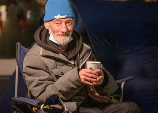 Ein Mann sitzt in einem Campingstuhl und hält einen Becher in der Hand
