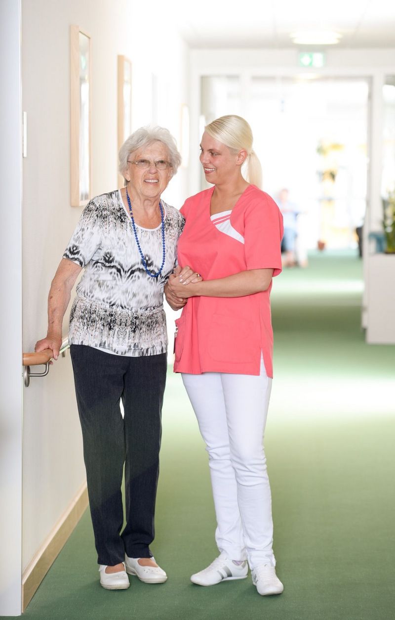 Eine ältere Frau wird von einer jungen Pflegerin gestützt