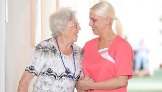 Mitarbeiterin der Malteser Pflegeeinrichtungen stützt ältere Frau bei ihrem Rundgang durch die Einrichtung. 