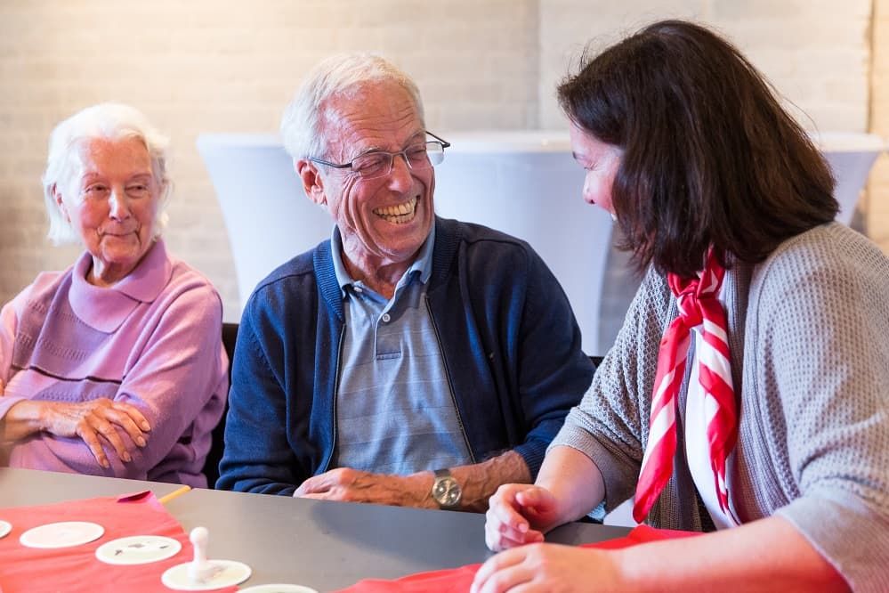 Zwei Senioren lachen mit einer Malteser Mitarbeiterin