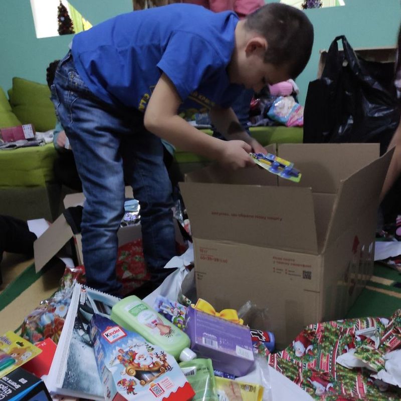 Ein Junge über einem Karton inmitten von Süßigkeiten und Geschenkpapier.