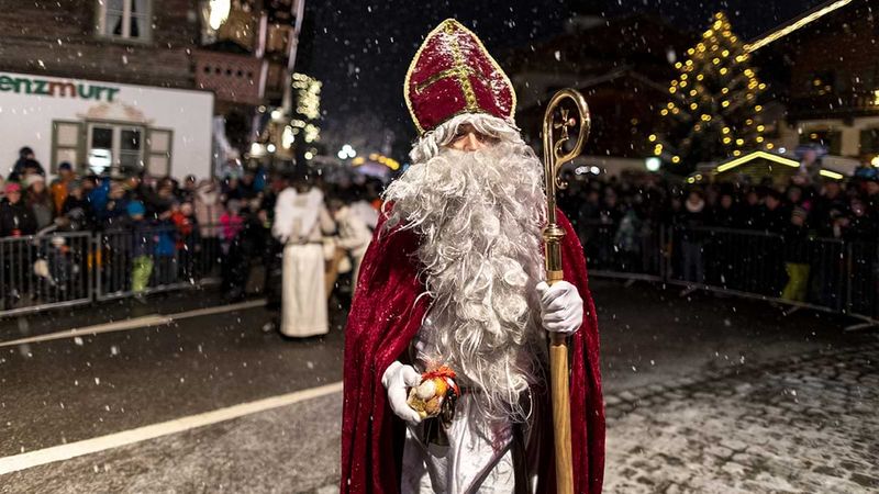 Ein als Nikolaus verkleideter Mann auf einer verschneiten Straße. Dahinter eine Menschenmenge.