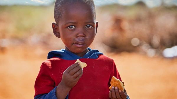 Es wird das Porträt eines afrikanischen Jungen gezeigt, welcher isst.