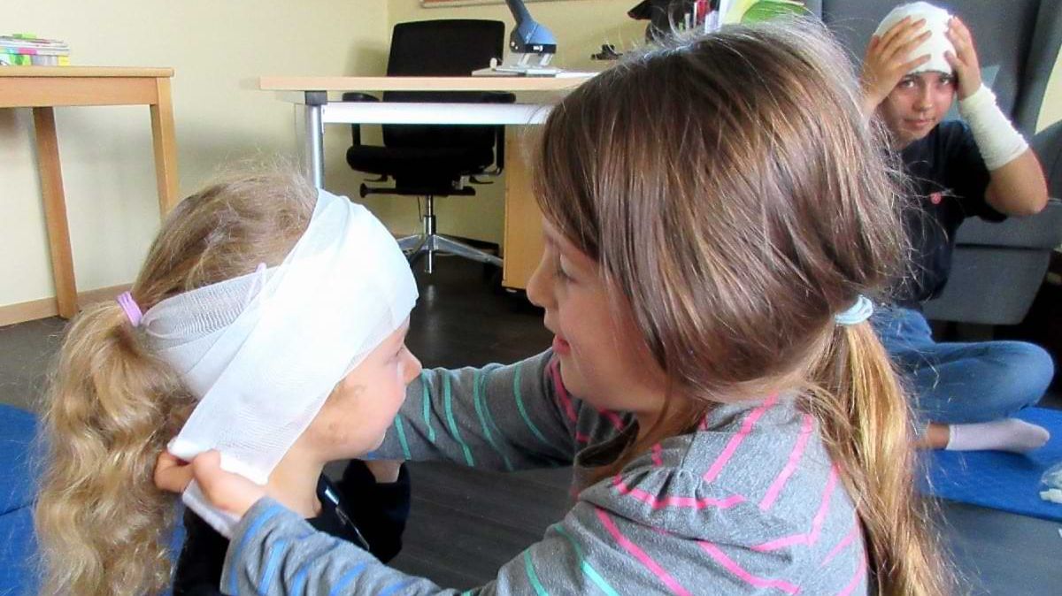 Ein junges Mädchen legt einem anderen Mädchen einen Kopfverband an.