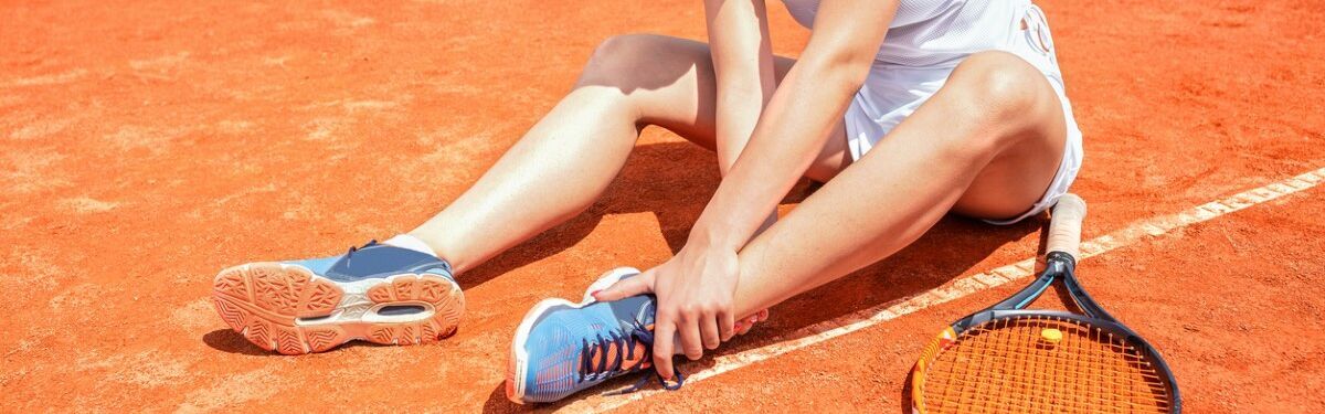 Junge Frau auf einem Tennisplatz hält sich den Fußknöchel mit schmerzverzerrtem Gesicht