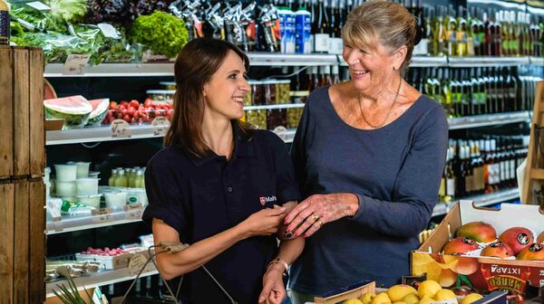 Malteser-Mitarbeiterin steht mit einer älteren Frau im Supermarkt.