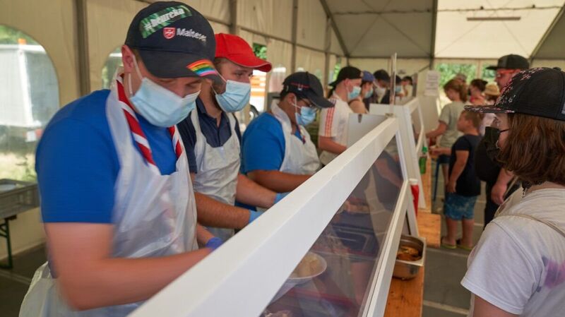 Mehrere junge Menschen mit Kappe und Maske geben Essen an einer Essensausgabe aus