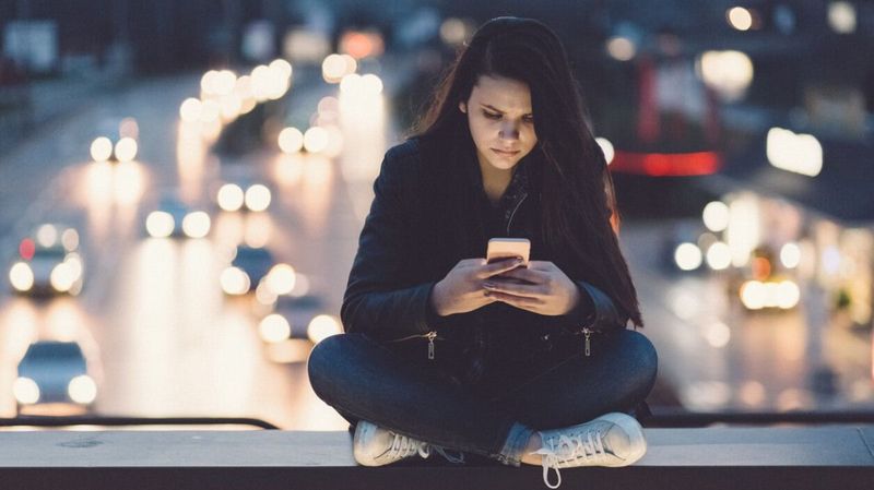 Mädchen mit Smartphone sitzt auf einer Autobahnbrücke