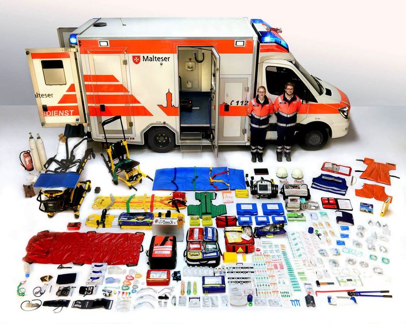 Ausrüstungsgegenstände eines Rettungswagens auf dem Boden vor einem Rettungswagen ausgebreitet. 