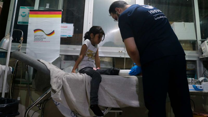 Ein kleines Mädchen mit bandagiertem Fuß wird auf einer medizinischen Liege von einem Mann untersucht