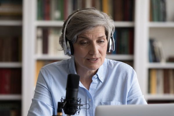 Eine ältere Frau mit Kopfhörern spricht in ein Mikrofon