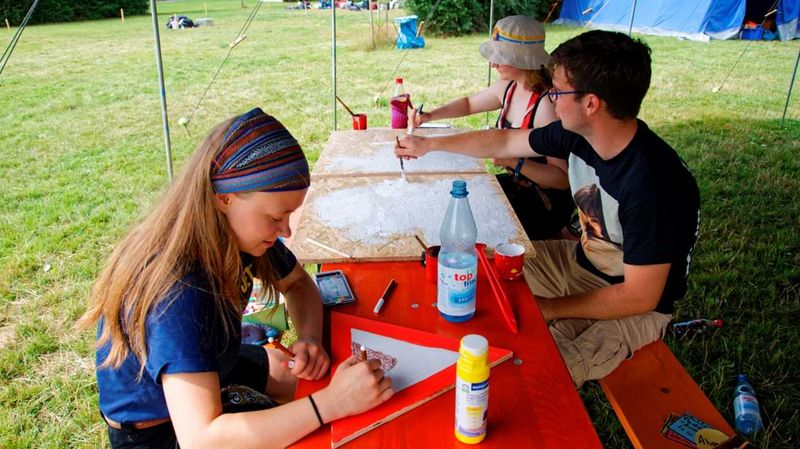 Junge Leute basteln und malen etwas an einem Tisch im Freien