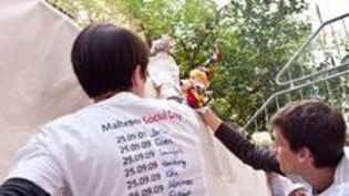 Zwei Jungen malen etwas auf ein Plakat. Sie tragen weiße T-Shirts mit der Aufschrift Social Day.
