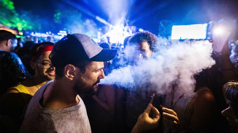 Menschen auf einem Festival, ein rauchender Mann mit Baseballmütze im Vordergrund